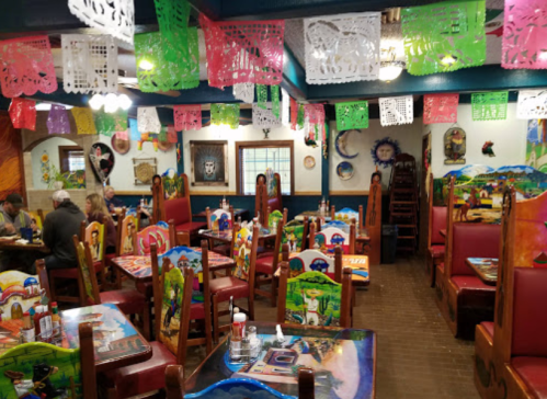 Colorful restaurant interior with decorated tables, vibrant papel picado banners, and patrons enjoying their meals.