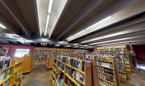 A spacious library interior with wooden bookshelves filled with books and bright overhead lighting.
