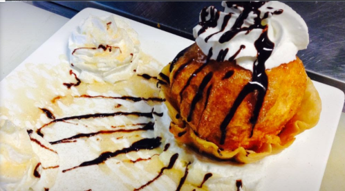 A dessert featuring a fried ice cream ball topped with whipped cream and chocolate drizzle, served with whipped cream on the side.