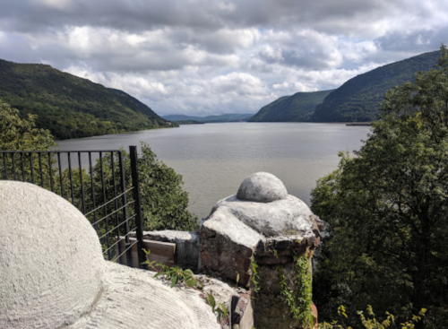 A scenic view of a river surrounded by hills, with cloudy skies and a stone structure in the foreground.