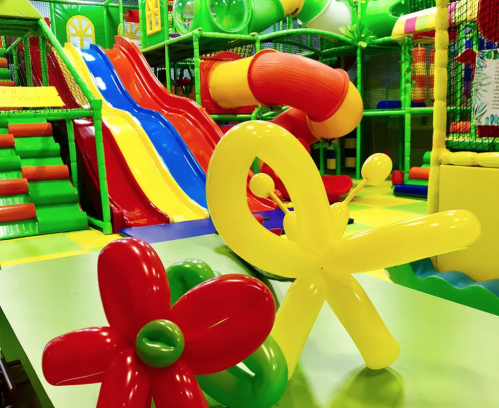 Colorful indoor play area with slides and tunnels, featuring balloon sculptures of a flower and a butterfly.