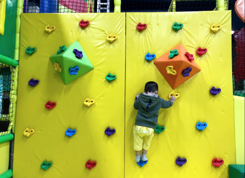 A child climbs a colorful indoor climbing wall with various grips in a playful environment.