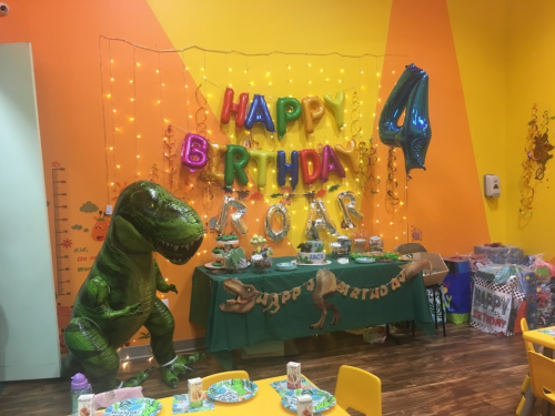 Colorful birthday party setup with dinosaur decorations, balloons, and a "Happy Birthday" banner for a 4th birthday celebration.