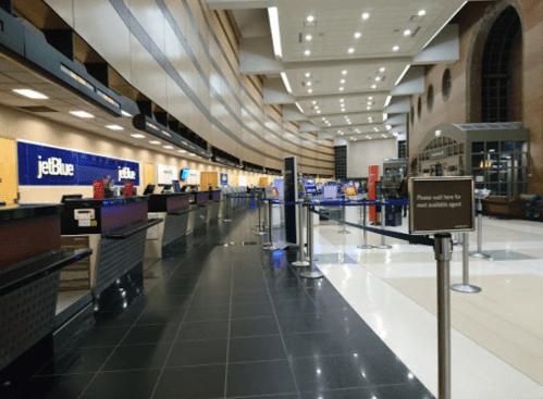 JetBlue check-in area at an airport, featuring empty counters and a sign instructing to wait for assistance.
