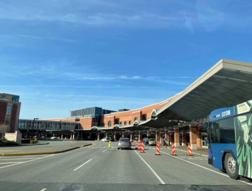 View of an airport entrance with a bus, traffic cones, and a clear blue sky in the background.