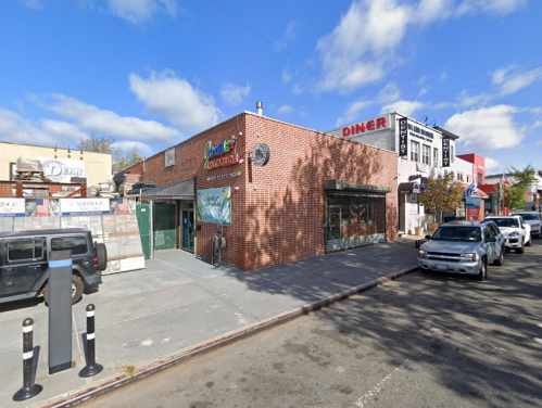 A street view of a brick building with a restaurant and diner, surrounded by parked cars and a clear blue sky.