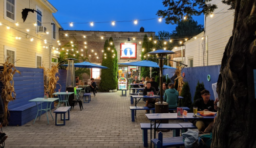 Outdoor dining area with string lights, blue tables, and patrons enjoying their meals in a cozy atmosphere.