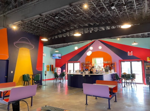 Colorful interior of a bar with a UFO mural, seating areas, and a well-stocked bar in the background.