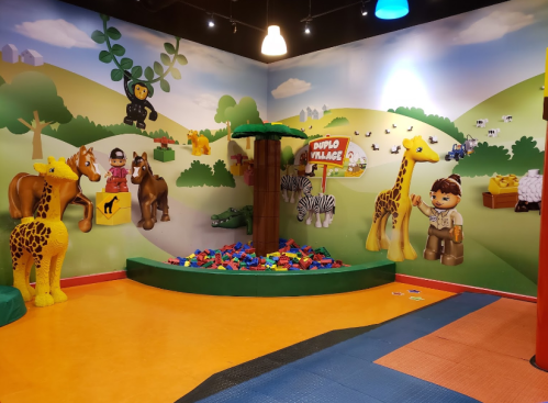 Colorful children's play area featuring animal figures, a tree, and a variety of building blocks on the floor.