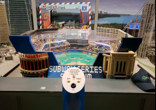 A miniature model of a stadium with a control panel, featuring colorful seating and a scenic backdrop of a city.