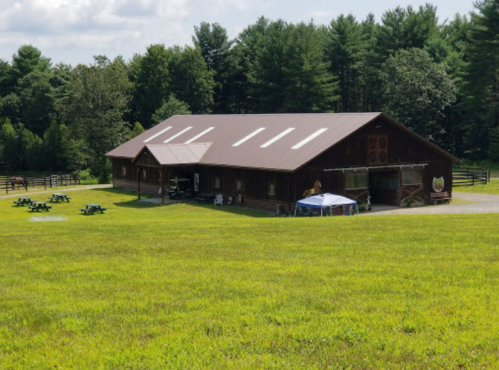 A large wooden building surrounded by green grass and trees, with picnic tables in the foreground.