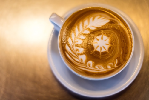 A close-up of a latte with intricate foam art featuring a star and leaf design in a white cup on a saucer.