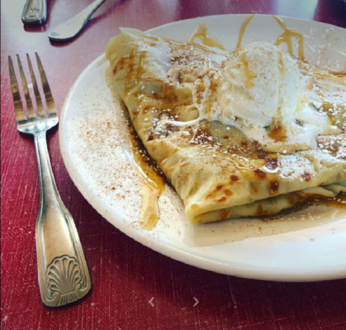 A plate of crepes topped with ice cream, caramel drizzle, and a sprinkle of cinnamon, with a fork beside it.