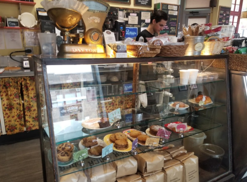 A display case filled with various baked goods, with a barista working in the background of a cozy café.