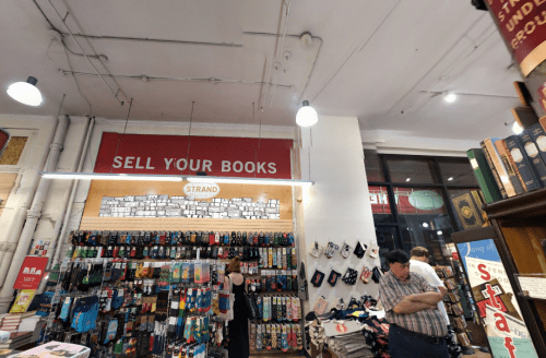 Interior of a bookstore featuring a "Sell Your Books" sign, shelves of socks, and customers browsing.