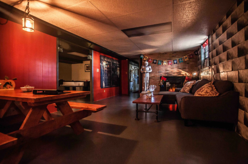 Cozy interior with a fireplace, seating area, and picnic table, decorated with festive banners and warm lighting.