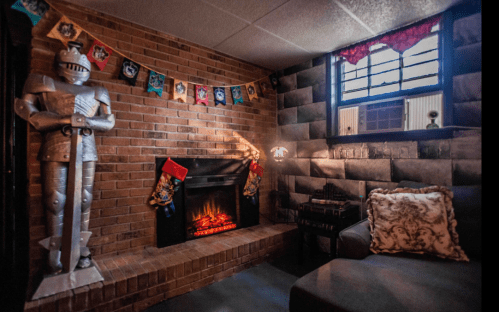 Cozy room with a brick wall, a knight statue, a fireplace, and festive decorations.