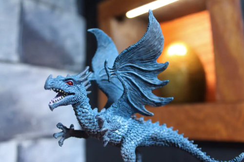 A detailed blue dragon figurine with wings spread, set against a textured stone background and a warm light.