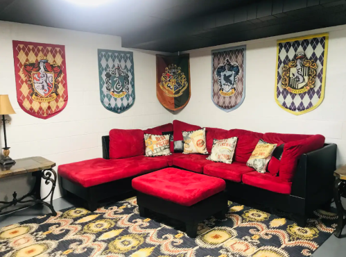 Cozy living room with a red sectional sofa, decorative pillows, and house banners on the wall.