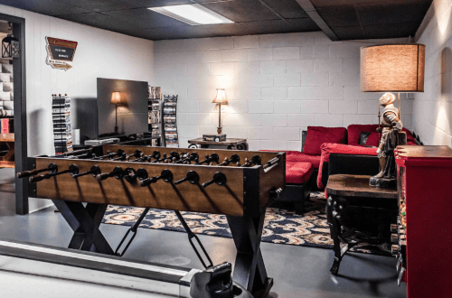 A cozy game room featuring a foosball table, red couch, lamp, and entertainment center against a white wall.