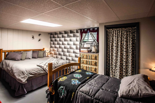Cozy basement bedroom with a queen bed, twin bed, bookshelf, and decorative window curtains.