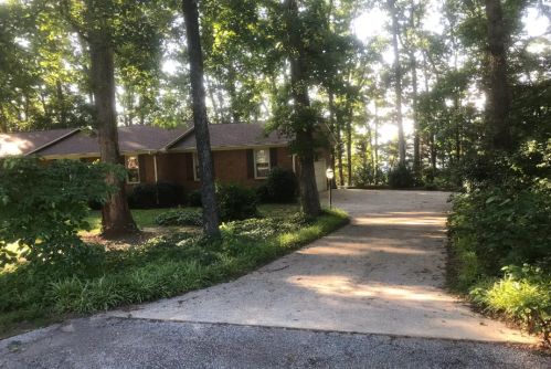 A brick house surrounded by trees, with a gravel driveway leading up to it in a wooded area.