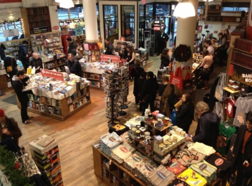 A busy bookstore filled with shoppers browsing books and gifts, with festive decorations and a warm atmosphere.