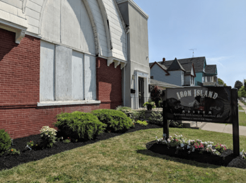Exterior of Iron Island, a brick building with a sign, surrounded by landscaped gardens and a clear blue sky.