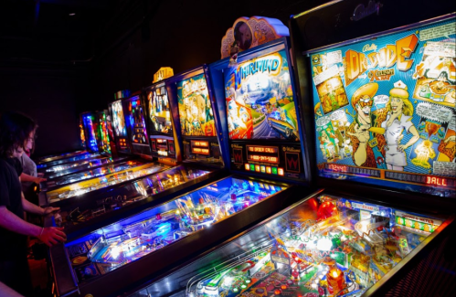 A row of colorful pinball machines with players engaged in a lively arcade setting.