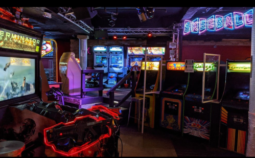 A vibrant arcade featuring classic games, neon lights, and a skeeball area, creating a nostalgic atmosphere.
