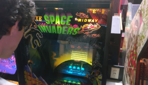 A person plays a retro Space Invaders arcade game, with colorful graphics and a glowing screen.