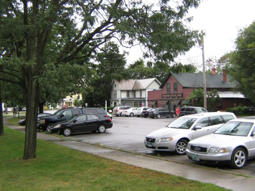 A parking lot with several cars, trees, and a building in the background on a cloudy day.