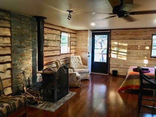 Cozy interior of a cabin with wooden walls, a stone fireplace, and comfortable seating by a door leading outside.