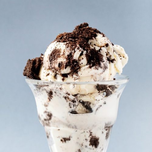 A glass dessert cup filled with creamy vanilla ice cream topped with crushed chocolate cookies.