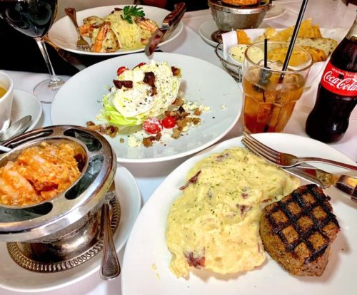 A table set with various dishes: grilled steak, creamy mashed potatoes, shrimp, salad, and drinks.