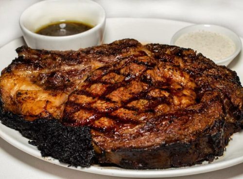 A juicy grilled steak on a plate, served with dipping sauces.