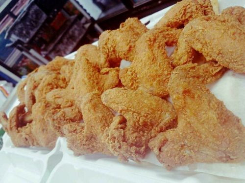 A close-up of golden-brown fried chicken wings arranged neatly on a white tray.