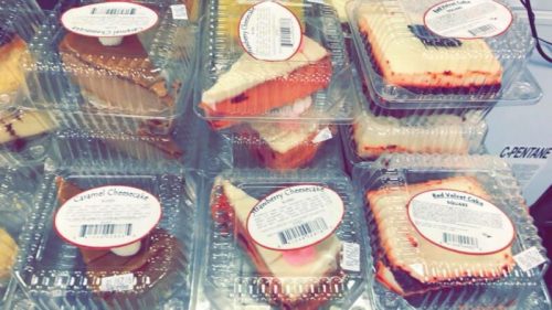 A display of assorted cheesecake slices in clear containers, including caramel and strawberry flavors.