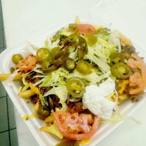 A takeout container filled with loaded fries topped with ground beef, cheese, lettuce, tomatoes, jalapeños, and sour cream.