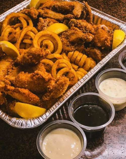 A tray of crispy fried chicken with curly fries and lemon wedges, accompanied by various dipping sauces.