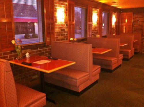 Cozy restaurant interior with pink booths, wooden accents, and warm lighting, featuring tables set for dining.