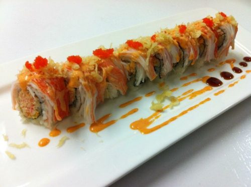 A plate of sushi rolls topped with crab, spicy sauce, and garnished with red fish roe and crispy flakes.