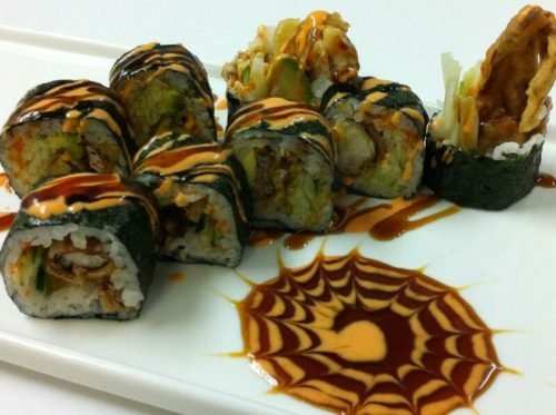 A plate of sushi rolls with various fillings, drizzled with sauce, and a decorative sauce design on the side.