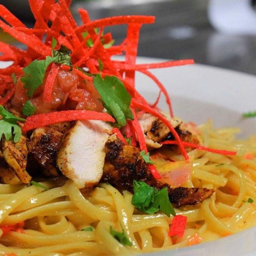 A plate of pasta topped with grilled chicken, salsa, and red strips, garnished with fresh cilantro.