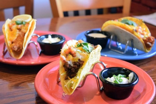 Two colorful plates with tacos in stands, one with beef and the other with chicken, served with dipping sauces.