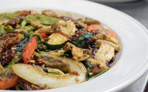 A colorful dish of sautéed vegetables, including zucchini, carrots, and mushrooms, served in a white bowl.