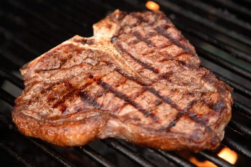 A perfectly grilled steak with a charred, crosshatch pattern, resting on a barbecue grill.