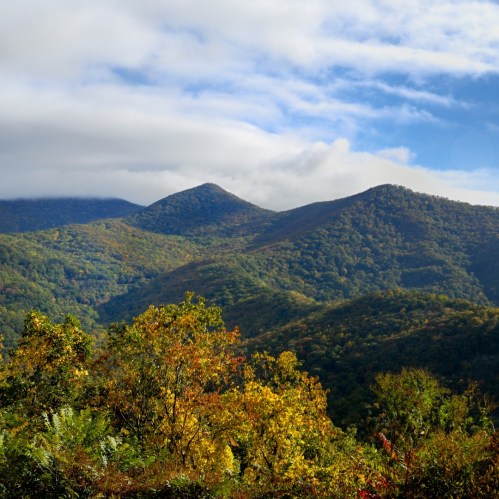 Scenic view of rolling mountains covered in autumn foliage under a partly cloudy sky.