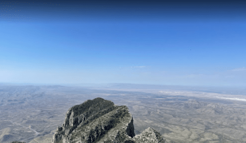 A panoramic view from a mountain peak, showcasing vast desert landscapes under a clear blue sky.