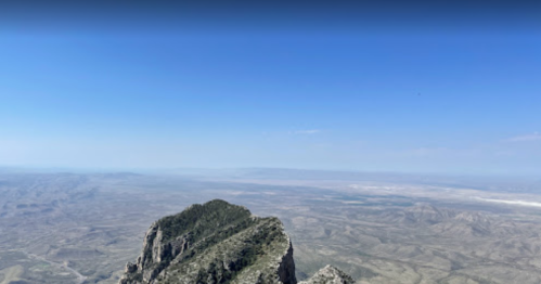 A panoramic view from a mountain peak, showcasing vast, arid landscapes under a clear blue sky.